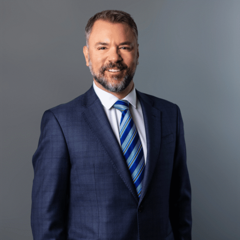 Portrait of Matthew Graham in a navy suit and blue striped tie