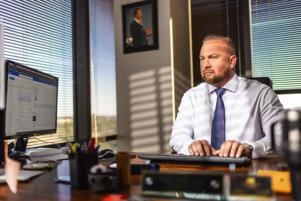 An attorney typing at his desk computer in a J. Alexander Law Firm office, with afternoon light coming through the window blinds
