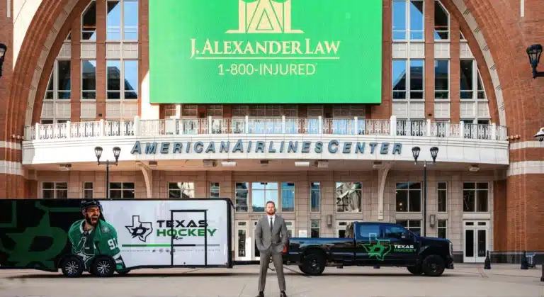 The American Airlines Center entrance in Dallas, with J. Alexander Law and 1-800-INJURED on the arena’s video screen and Josh Alexander standing beside a Dallas Stars trailer