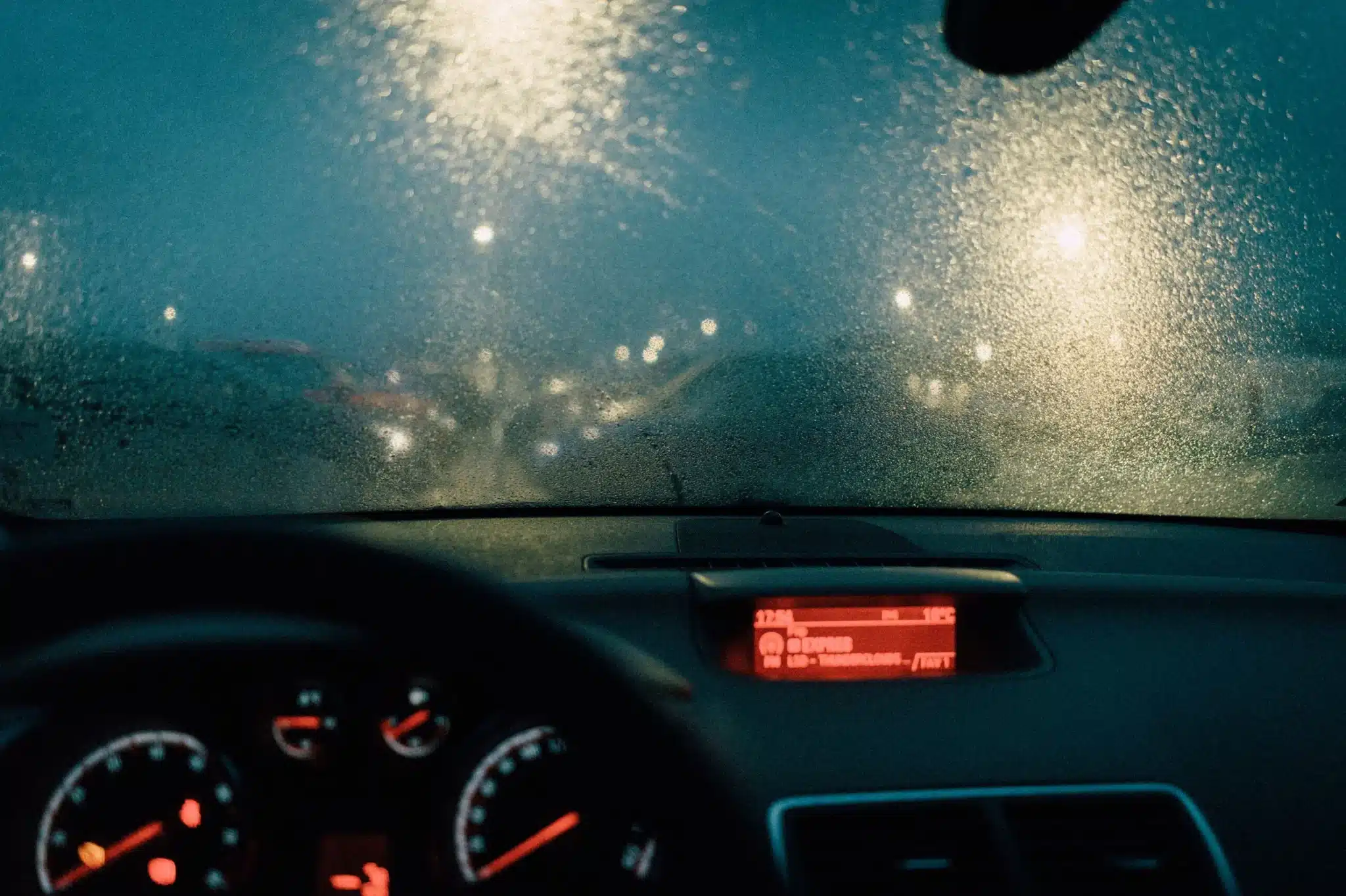 View through a rain-covered windshield at night with blurred lights ahead