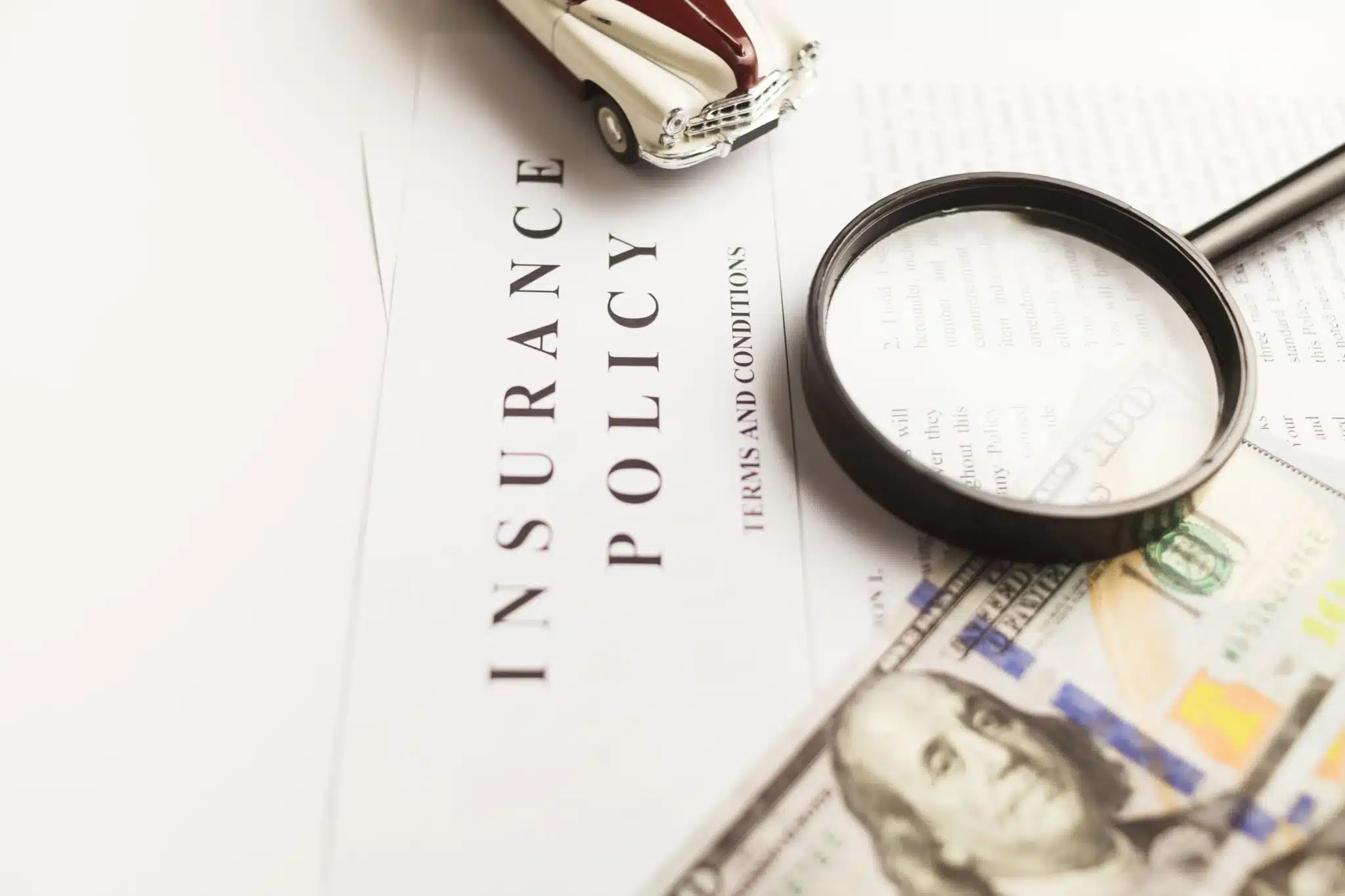Insurance policy document under a magnifying glass with cash and a toy car