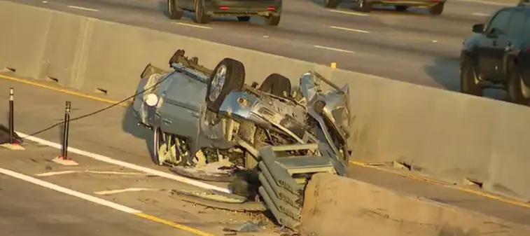 An SUV resting on its roof against the center barrier on US 75