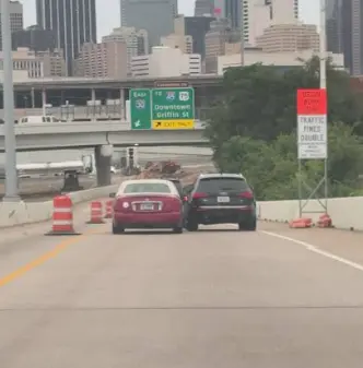 Two vehicles side by side on a narrowed Dallas roadway, downtown skyline ahead