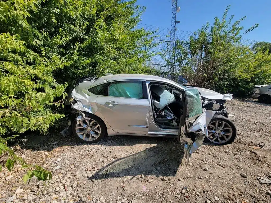 Side view of the client's silver sedan with crushed front and rear corners and a front door hanging open