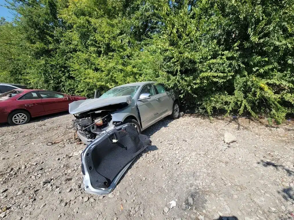 The client's silver sedan with a crushed front end and its detached trunk lid lying on the ground in front of it