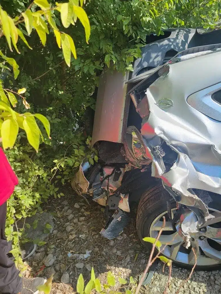 Close view of crumpled and torn silver bodywork and debris beside a wheel of the client's sedan