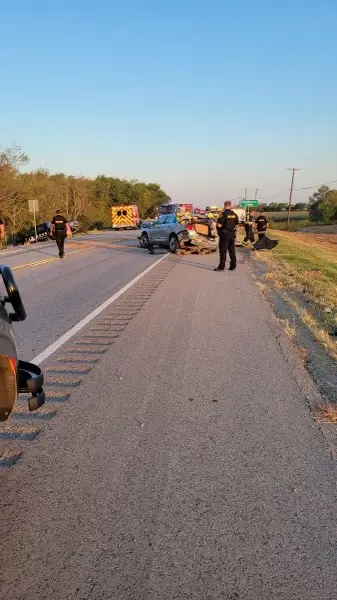 Law enforcement officers, emergency vehicles, and a damaged silver car on the highway at the crash scene
