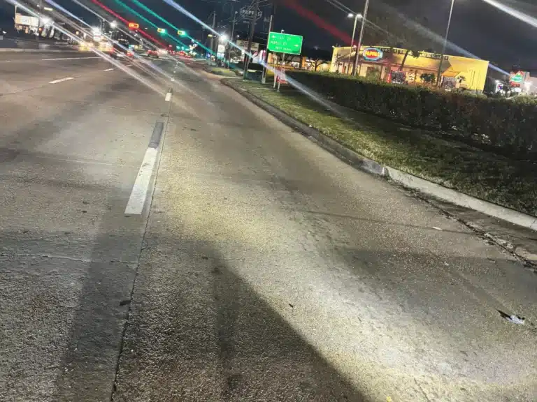 Eastbound FM 1960 West at night with debris scattered on the right lane and the Raising Cane's building beyond the curb