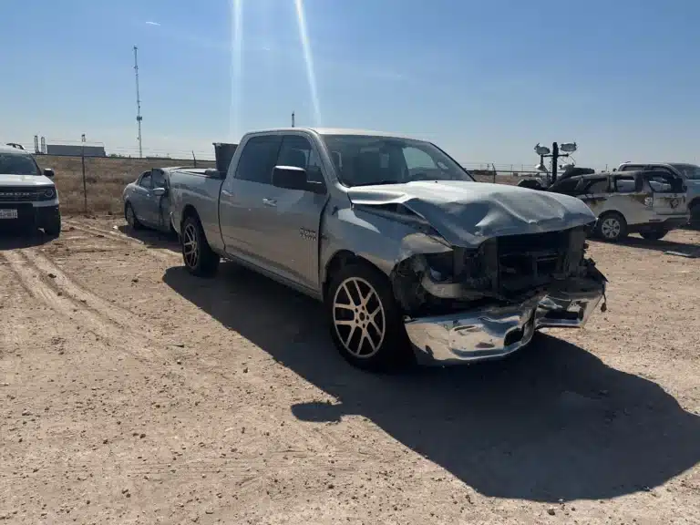 The client's silver pickup seen from the right front in the storage lot, with the hood crumpled and the right headlight and bumper torn away