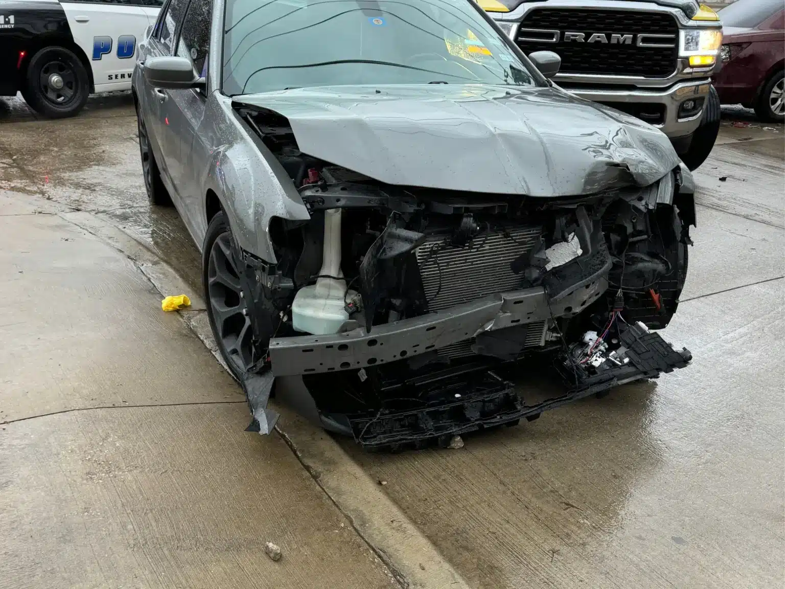 El Chrysler plateado de nuestro cliente, con la parte delantera destrozada tras el accidente en Abrams Road, en Dallas, y con vehículos policiales detenidos detrás de él