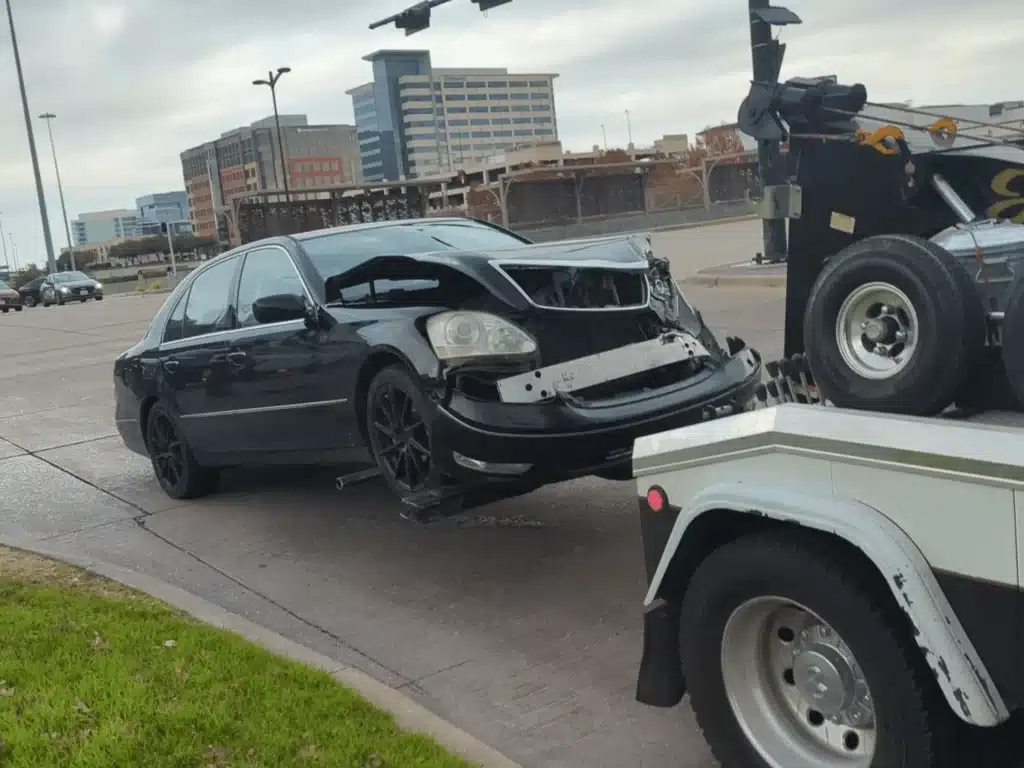Our client's black Lexus with a crumpled front end being loaded onto a tow truck after the Plano crash