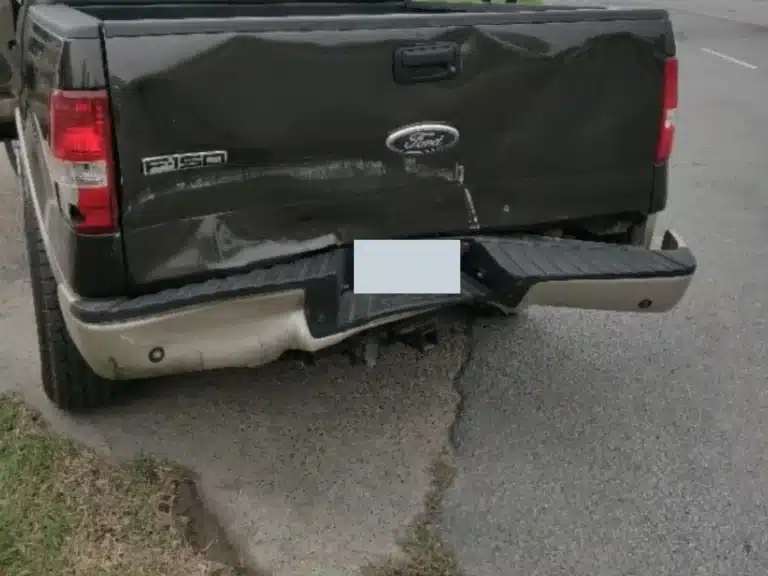 Rear view of the family's dark green Ford F-150 after the crash, its tailgate creased and dented and the rear bumper bent inward below the Ford badge