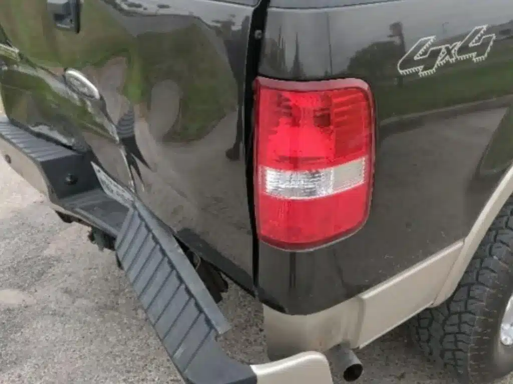 Close view of the F-150's rear corner with the tail lamp, the creased edge of the tailgate and the bumper step bent downward