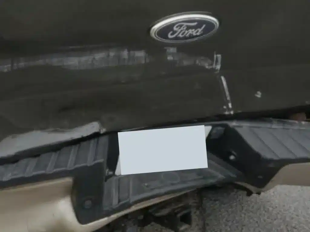 Close view of scrapes and dents across the F-150 tailgate beneath the Ford badge, with the bent rear bumper below