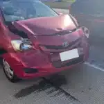 The striking red sedan with a crumpled hood, a front bumper pushed inward, and a cracked windshield