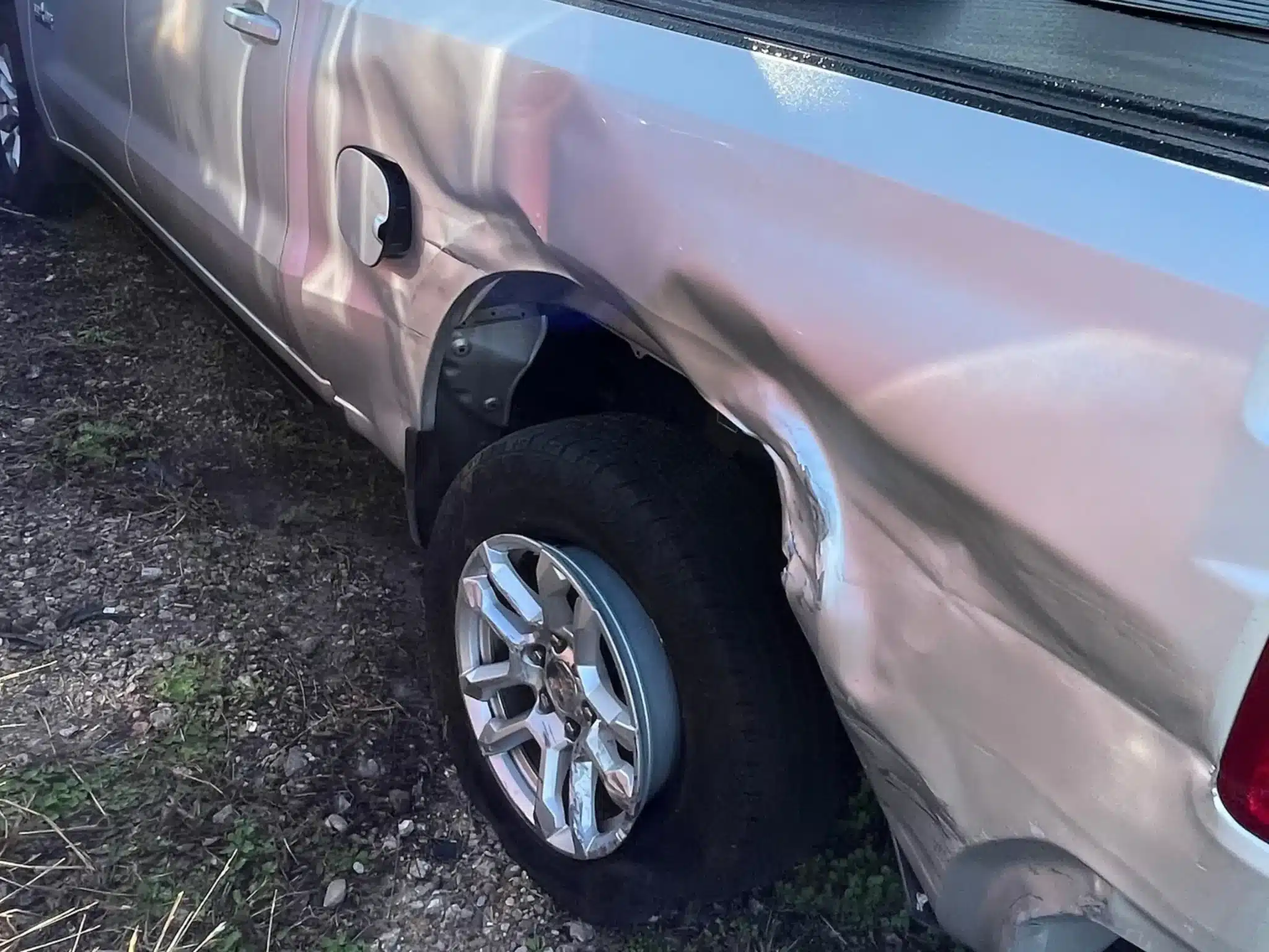 Crushed and deformed rear driver-side bed panel and wheel area of the client's Chevrolet Silverado after the Pasadena crash