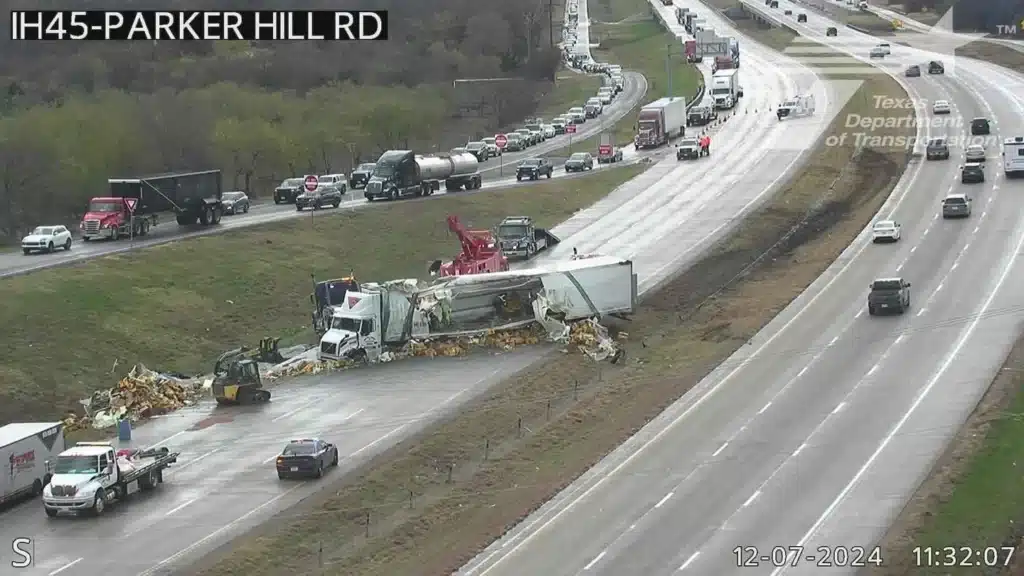 TxDOT traffic camera view of the same stretch of I-45 later that morning, wreckers lifting the damaged trailer while its load lies scattered across the closed northbound lanes