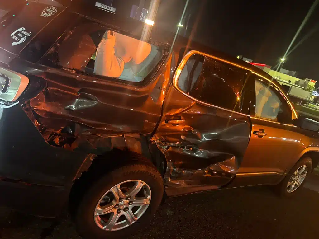 El SUV de nuestra clienta de noche, despu&eacute;s del accidente en La Porte, con la puerta trasera derecha y el panel lateral trasero hundidos y una bolsa de aire de cortina desplegada que se ve por la ventana trasera rota