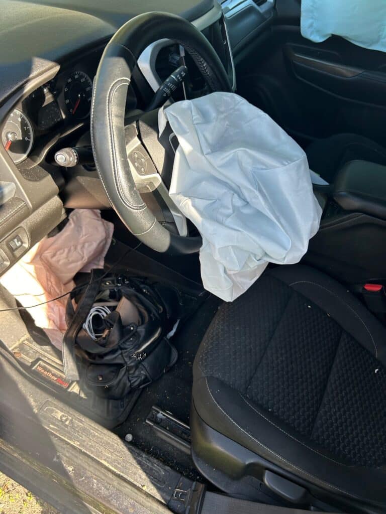 El asiento del conductor del SUV de nuestra clienta, con la bolsa de aire del volante desplegada y sus pertenencias en el piso