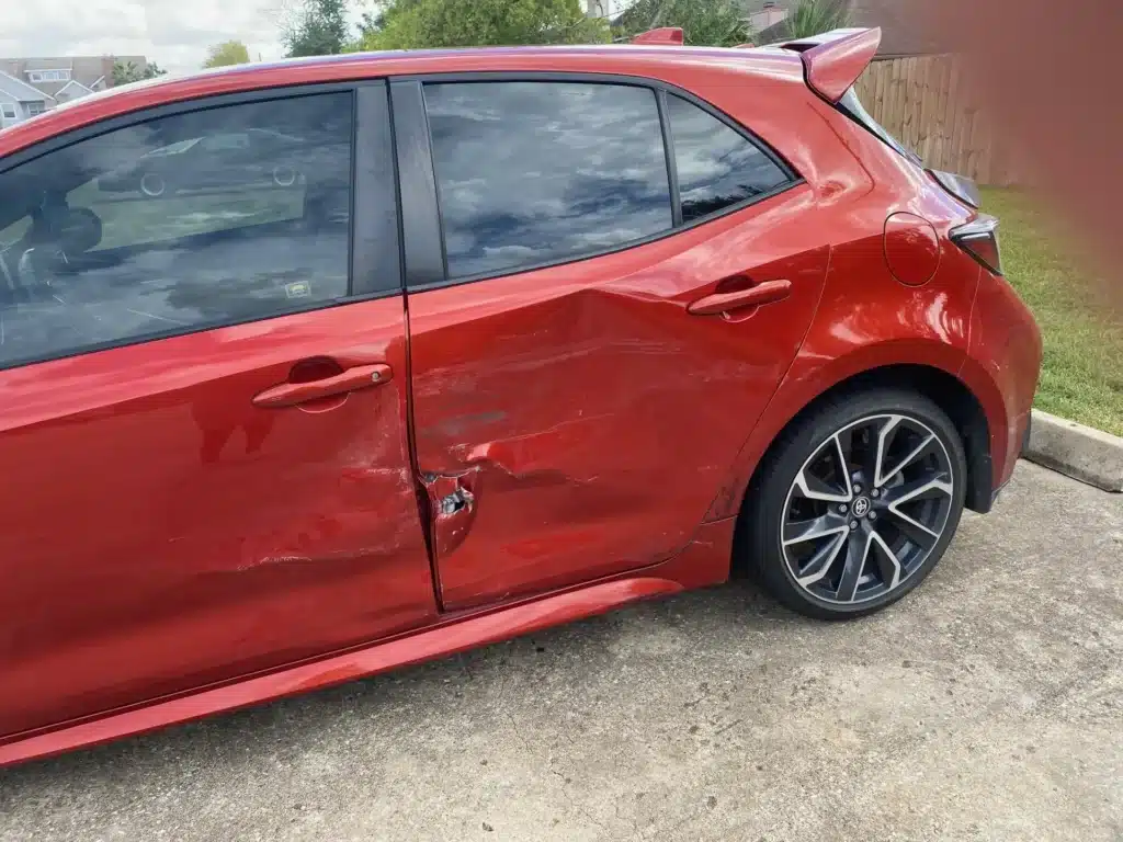 Vista cercana de la puerta trasera del lado del conductor y del panel lateral trasero abollados del hatchback rojo de nuestra clienta