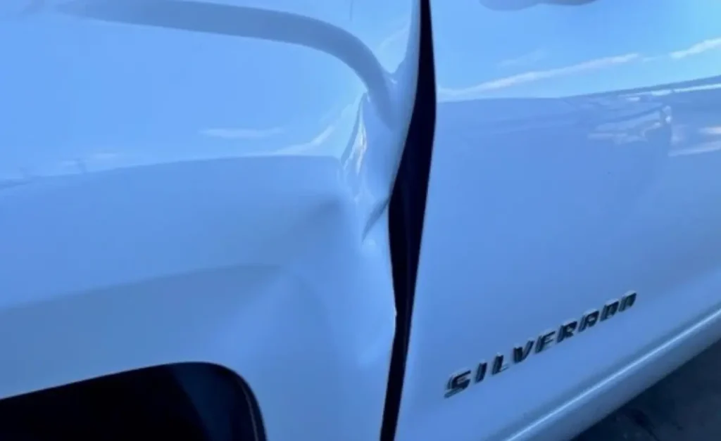The Silverado&rsquo;s front fender bent back where it meets the driver&rsquo;s door, beside the Silverado badge