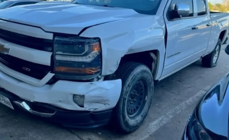 The front of our client's white Chevrolet Silverado after the Richardson crash, its bumper crushed and torn at the driver's side corner, the fender crumpled above the wheel and the hood pushed up