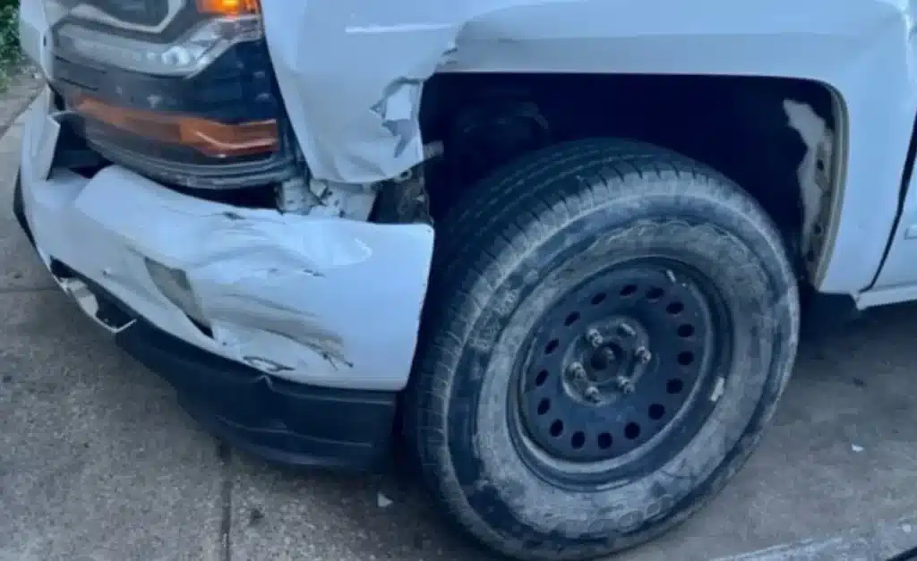 Driver&rsquo;s side front corner of the Silverado, the bumper cover torn and folded and the fender ripped open above the front wheel