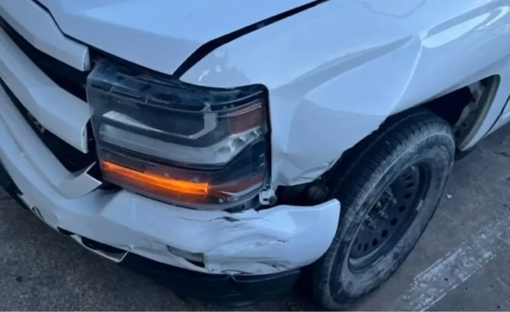 Close view of the Silverado&rsquo;s driver side headlight knocked out of place, the hood creased and the fender pushed in behind it