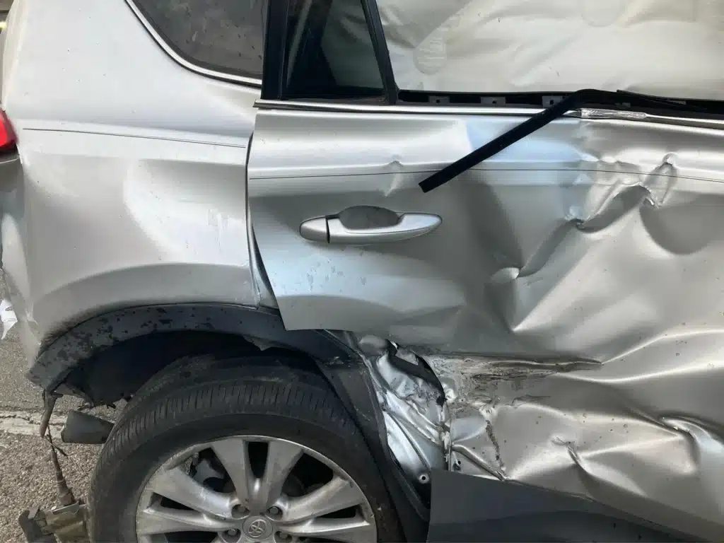 Close view of the RAV4's caved in right rear door and crumpled rocker panel, beside the seat where one of our clients rode
