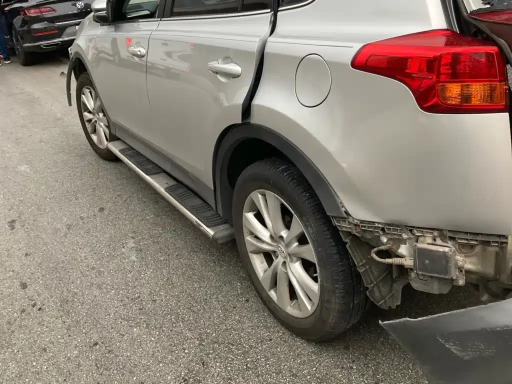 Left rear corner of the RAV4 with the bumper cover torn away, exposing the brackets and wiring underneath