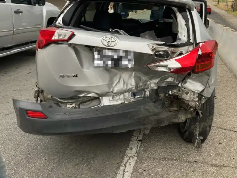 Rear of our clients' silver Toyota RAV4 on the I-35 exit ramp, its liftgate crushed inward, the rear glass gone and the bumper cover hanging loose