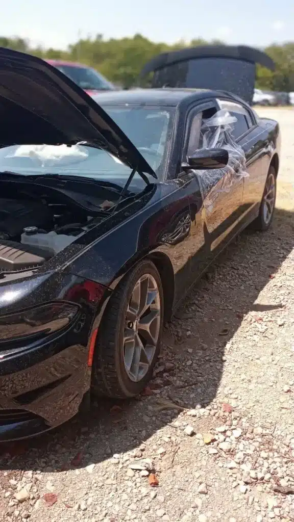 El lado del conductor del sed&aacute;n de nuestro cliente, con el cofre levantado y pl&aacute;stico pegado con cinta sobre una ventana, y el airbag desplegado por dentro