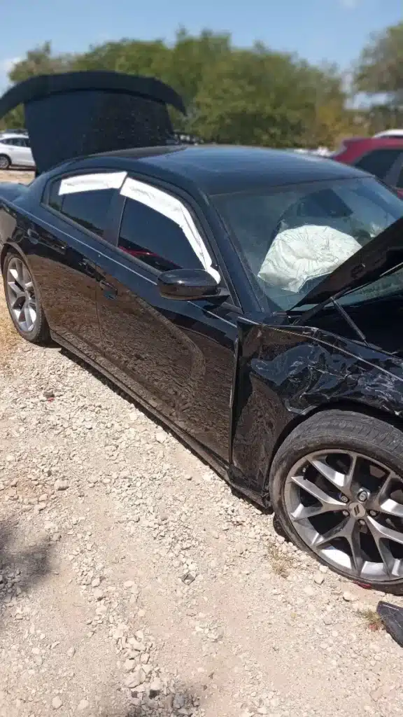 El sed&aacute;n negro de nuestro cliente despu&eacute;s del accidente en la se&ntilde;al de alto en DeSoto, con la salpicadera delantera del lado del pasajero aplastada y un airbag desplegado visible a trav&eacute;s del parabrisas