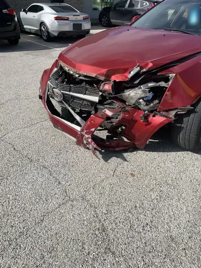 El auto rojo que sali&oacute; de la se&ntilde;al de alto, con el cofre abollado y la esquina delantera izquierda desgarrada, estacionado en un estacionamiento despu&eacute;s de la colisi&oacute;n