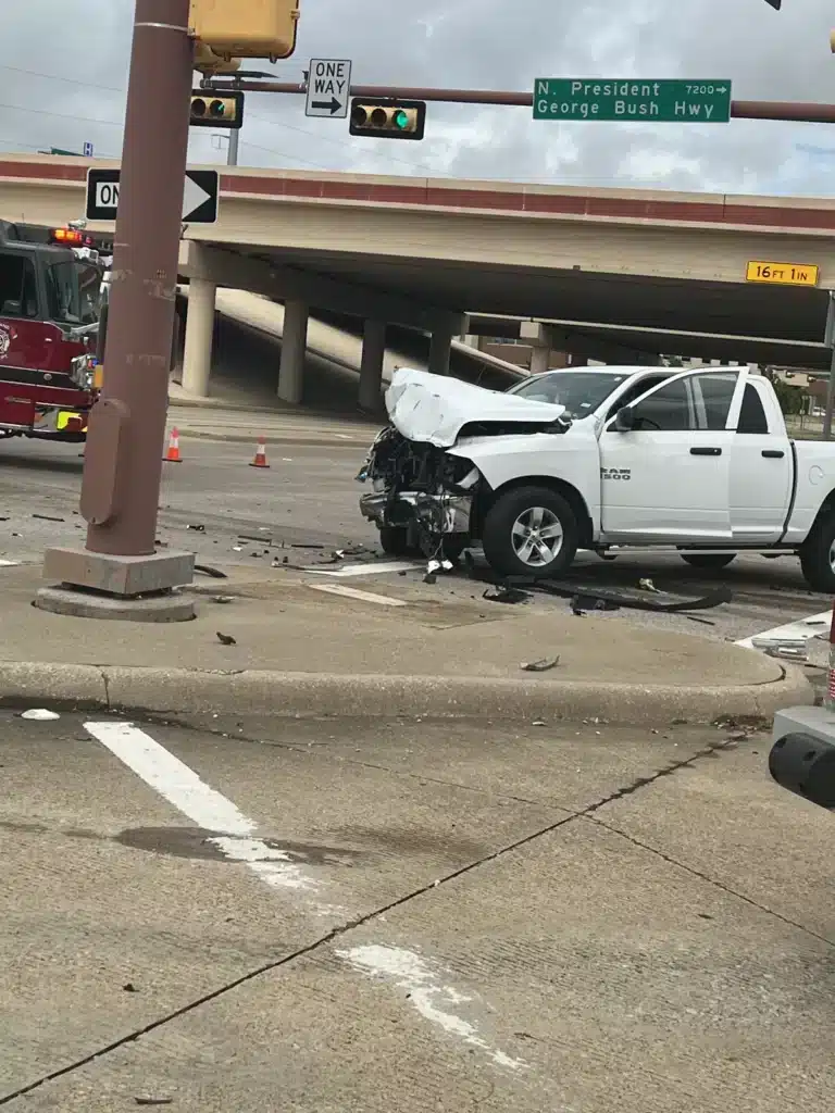 Camioneta pickup con el frente destrozado junto a un letrero de calle en una carretera, debajo de un paso elevado