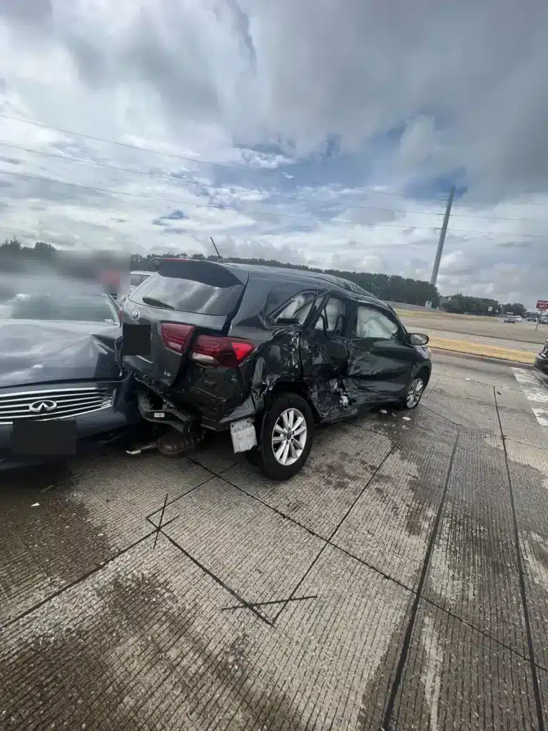 El lado del pasajero de la SUV oscura de nuestra clienta despu&eacute;s del accidente en el sem&aacute;foro en rojo, con ambas puertas aplastadas y las bolsas de aire de cortina colgando dentro de las ventanas