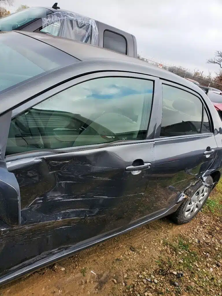 El lado del conductor del sed&aacute;n gris de nuestro cliente despu&eacute;s del accidente por la luz roja, con las dos puertas hundidas y el panel desgarrado arriba de la llanta trasera