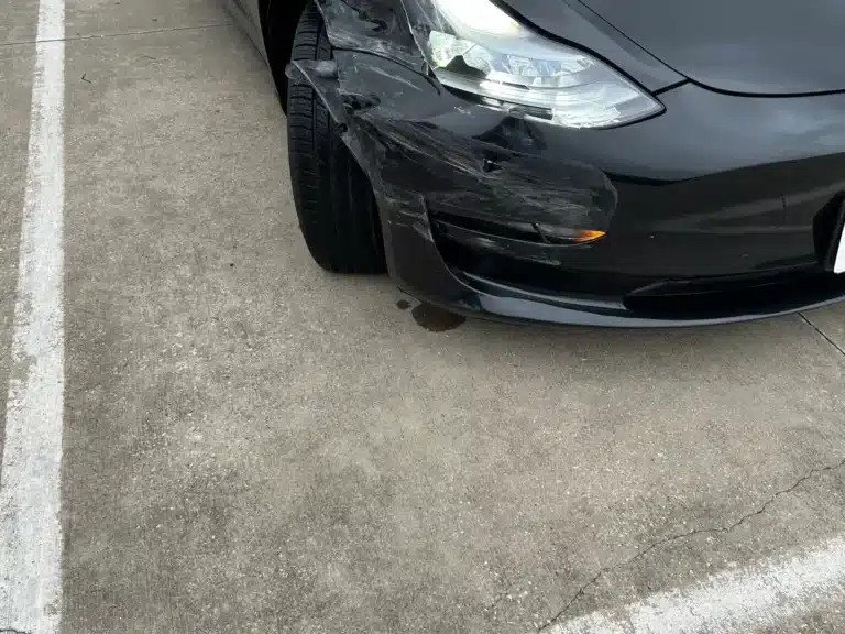 Our client's black Tesla Model 3 after the Farmers Branch crash, its front right corner crushed with the bumper cover torn back around the wheel, the headlamp cracked and the fender pushed in