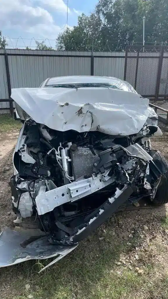 Parte delantera del sed&aacute;n blanco de nuestra clienta tras el choque frontal en la US 67, con el cofre doblado hacia arriba, el parachoques arrancado y el compartimento del motor aplastado