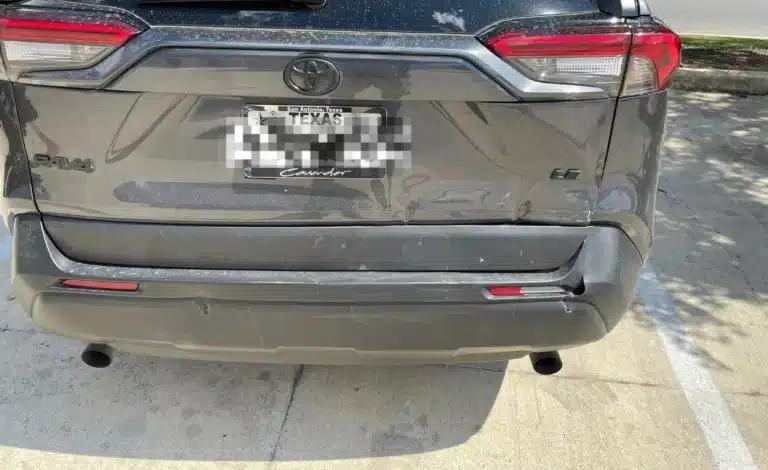 Rear of our client's gray Toyota RAV4 in the shopping center lot after the San Antonio crash, with the liftgate dented low on the passenger side and the bumper sitting slightly out of line