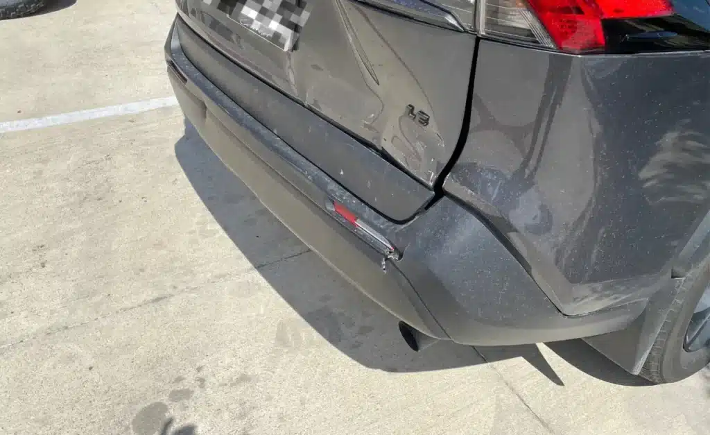 Close view of the RAV4&rsquo;s rear passenger side corner: a crease across the liftgate beside the badge and the bumper cover pulled away from the body; the plate is pixelated
