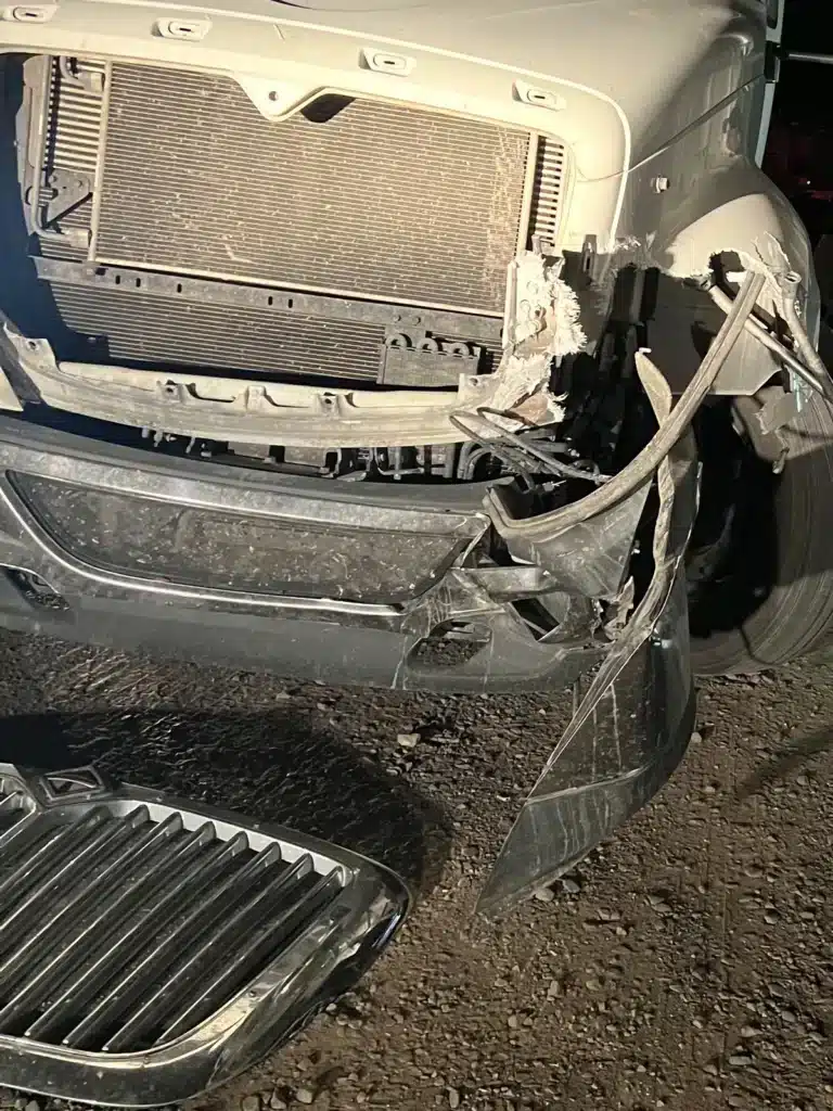El frente del tractocami&oacute;n blanco de nuestra clienta en el sitio del pozo esa noche, con la esquina del lado del conductor desgarrada, el parachoques doblado hacia abajo y la parrilla sobre la grava