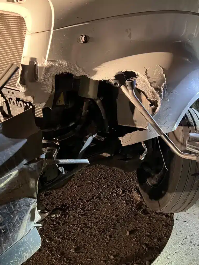 Salpicadera delantera rasgada del lado del conductor de un tractocami&oacute;n, con el cableado y el brazo del espejo colgando sobre la llanta